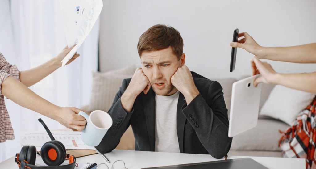 Many hands reach out to a man with various objects