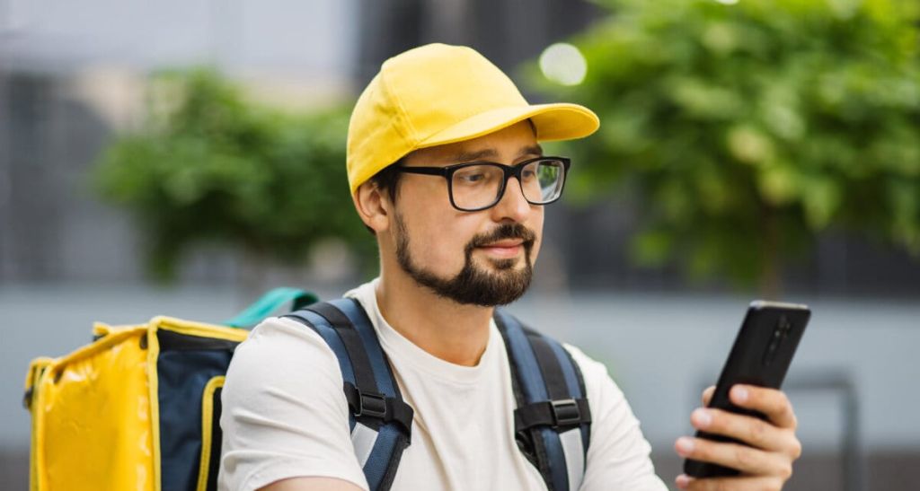 Caucasian man courier of food delivery with big thermal backpack on his back talking on smartphone